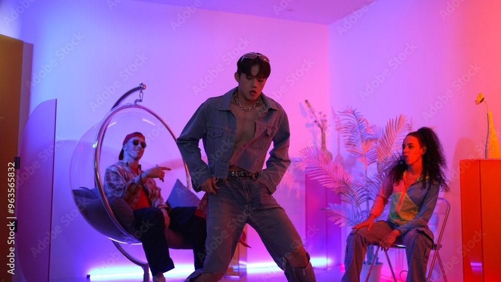 Fototapeta premium Skilled asian dancer moving to modern music while multicultural friend sitting at chair. Professional performer dancing show energetic foot step while hipster team cheering and supporting. Regalement.