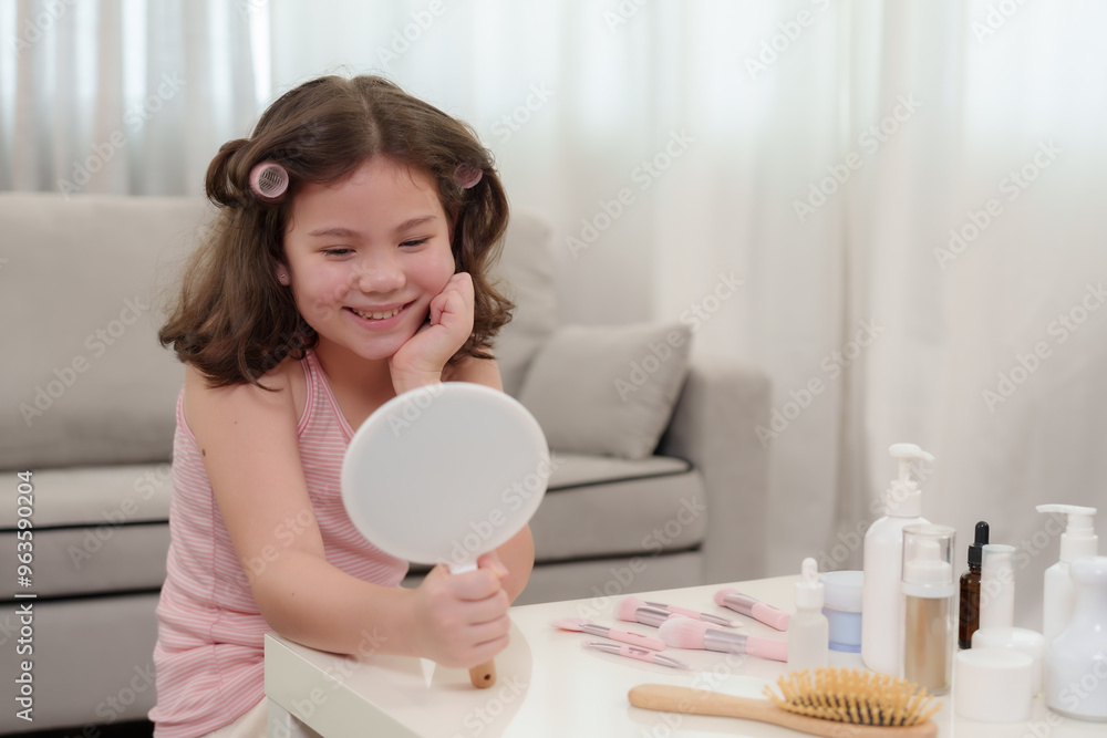 Young half-Asian girl smiling while looking in handheld mirror. Hair in soft rollers, surrounded by beauty products on white table. Expressing self-care and happiness during beauty routine at home. Young half-Asian girl smiling while looking in handheld mirror. Hair in soft rollers, surrounded by beauty products on white table. Expressing self-care and happiness during beauty routine at home.