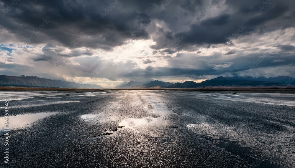open flat area of asphalt with puddles, rain, and distant mountains