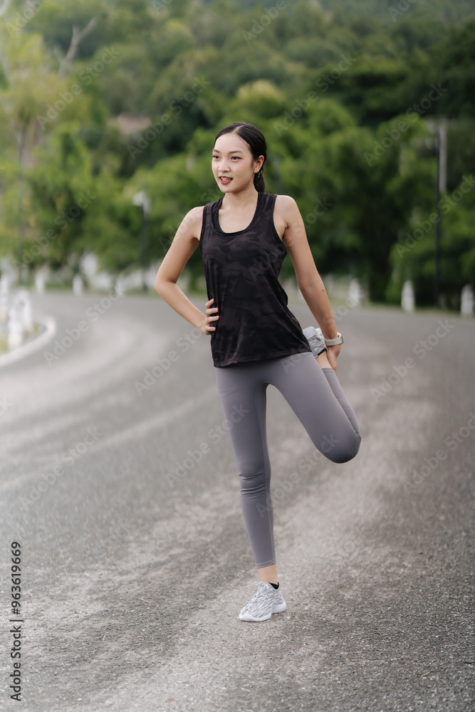 Morning Stretch on Winding Road: A woman in athletic wear performs a leg stretch on a winding road, surrounded by lush greenery. Her confident posture and serene expression embody the peace and focus Morning Stretch on Winding Road: A woman in athletic wear performs a leg stretch on a winding road, surrounded by lush greenery. Her confident posture and serene expression embody the peace and focus