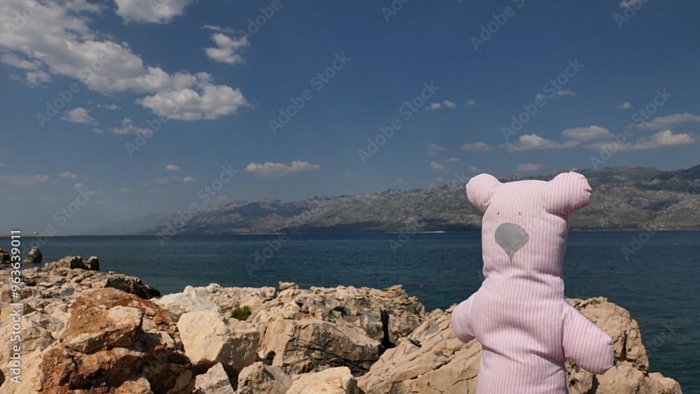 Φωτογραφία Cute handmade slim teddy made of fabric with thin pink vertical lines is looking at Croatian bay near city of Razanac, with Velebit mountain in background