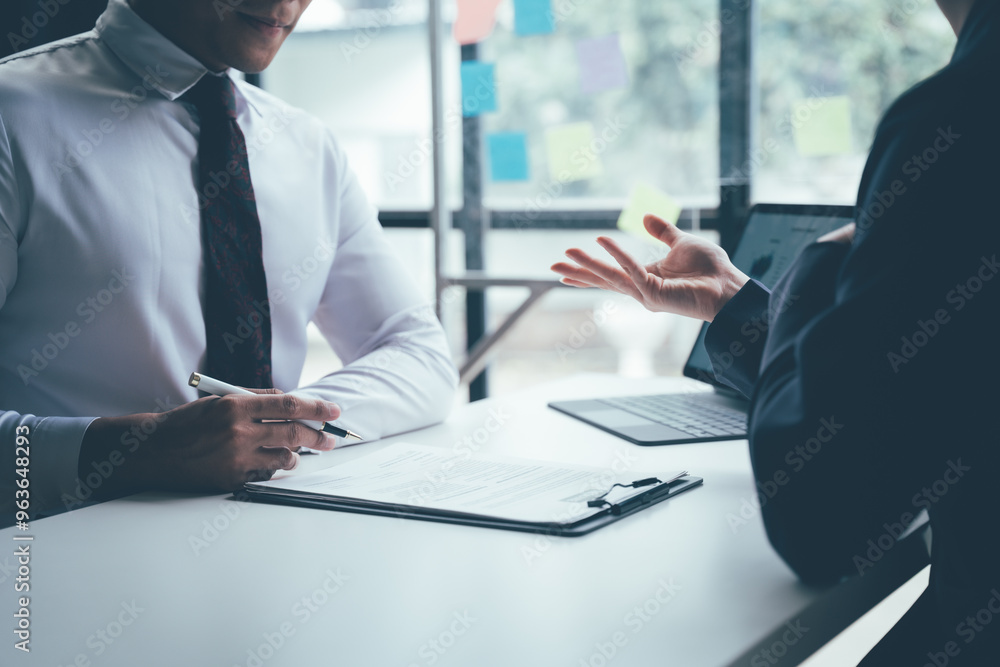 Negotiating the Deal: Two business professionals engaged in focused discussion, reviewing a contract at a modern office desk. Negotiating the Deal: Two business professionals engaged in focused discussion, reviewing a contract at a modern office desk.