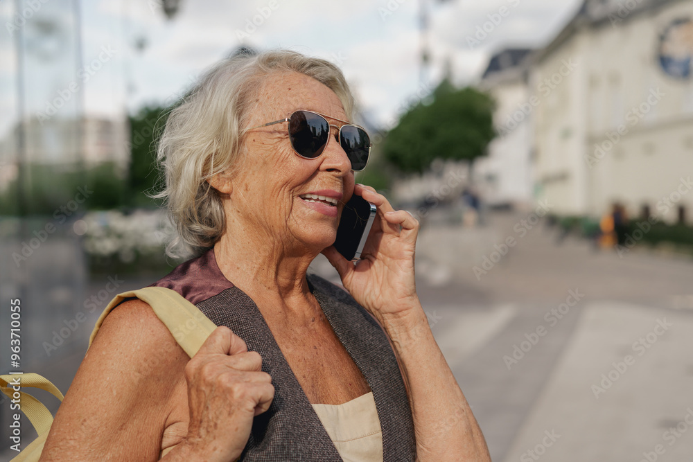 A joyful elderly woman happily chats on her smartphone while taking a leisurely stroll through a vibrant urban setting A joyful elderly woman happily chats on her smartphone while taking a leisurely stroll through a vibrant urban setting