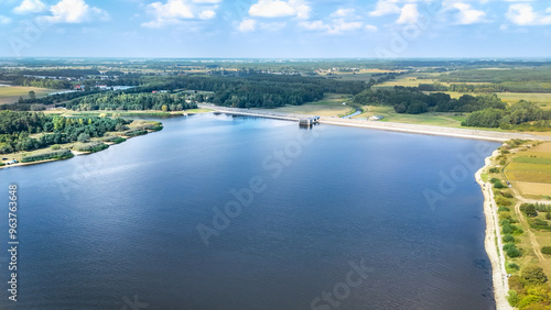 Wallpaper Mural A scenic aerial view of a reservoir with a dam, surrounded by lush green fields and forests. The calm water reflects the sky, and the countryside stretches towards the horizon under a clear sky. Torontodigital.ca