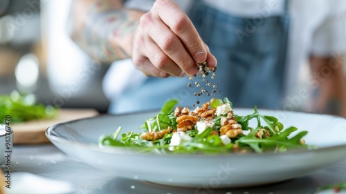 A tattooed hand sprinkles pink peppercorns onto a salad of arugula, goat cheese, and walnuts.