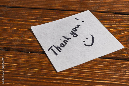 A thank you note is written on a piece of paper and placed on a wooden surface.