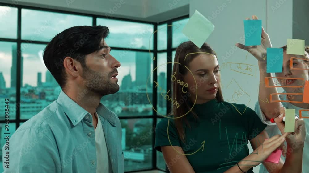 Professional business team brainstorm, sharing, thinking idea while skilled male leader write on sticky notes at glass wall. Skilled manager placed business plan on glass wall at office. Tracery