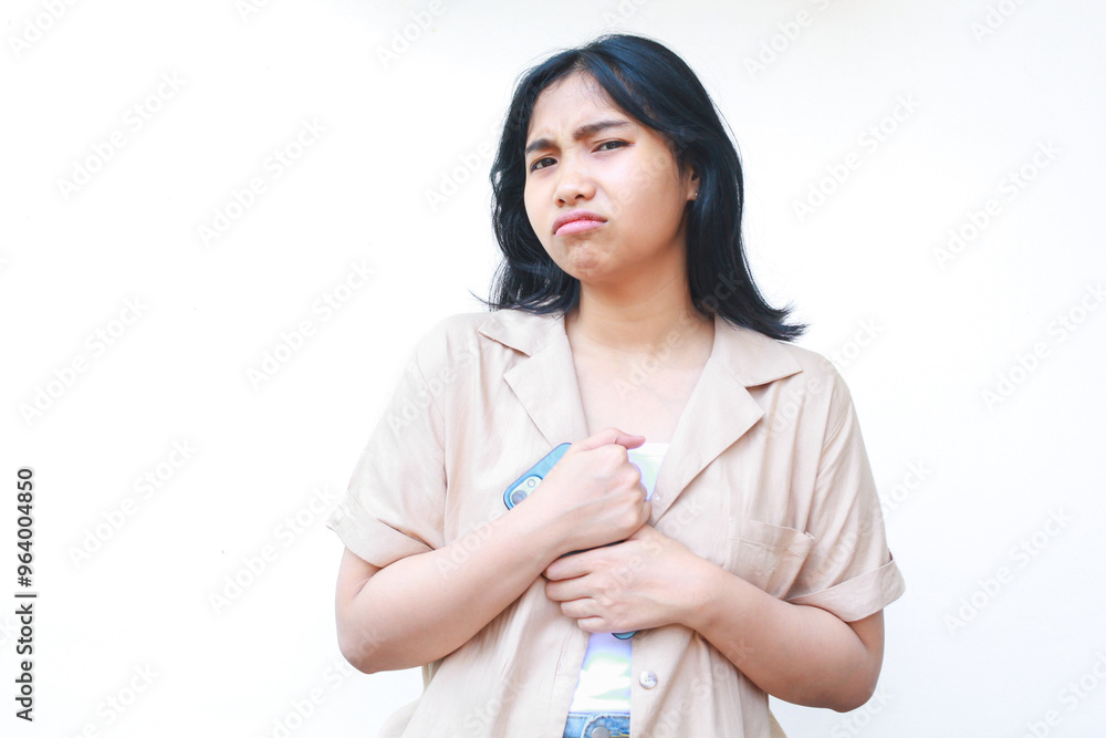 irritated asian woman holding smartphone over her chest wearing casual clothes isolated on white background, look at camera irritated asian woman holding smartphone over her chest wearing casual clothes isolated on white background, look at camera