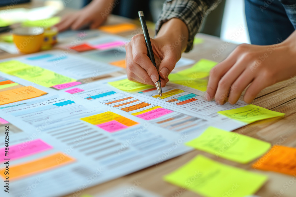 Brainstorming business plans with sticky notes and sketches on wooden table. hands are actively engaged in writing and organizing ideas. Brainstorming business plans with sticky notes and sketches on wooden table. hands are actively engaged in writing and organizing ideas.