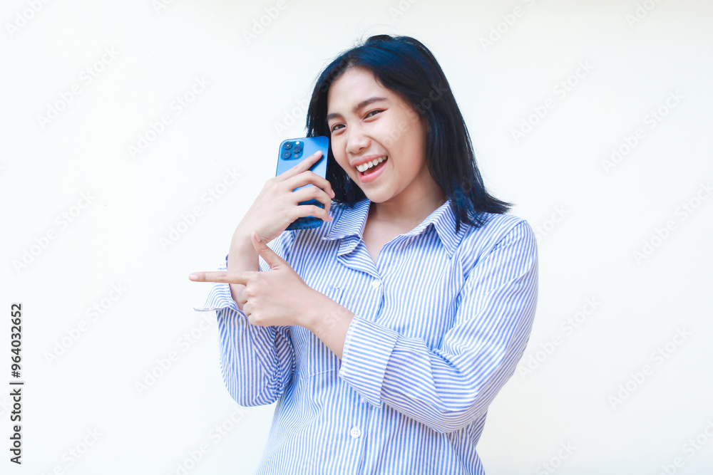 excited asian woman talking on smartphone and pointing finger show presenting gesture wearing striped shirt isolated on white background