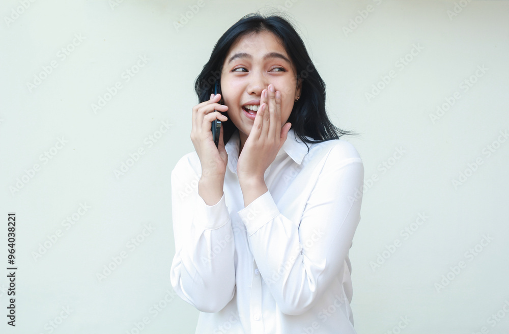 image of delighted asian young woman secretary speaking on smartphone looking away covering mouth with palms feeling shy talking gossip whispering wearing white formal suit shirt standing isolated image of delighted asian young woman secretary speaking on smartphone looking away covering mouth with palms feeling shy talking gossip whispering wearing white formal suit shirt standing isolated