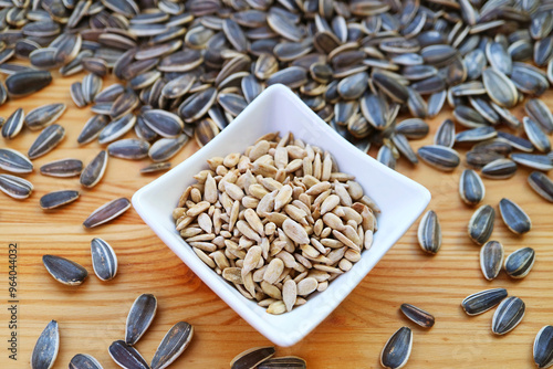 Bowl of roasted sunflower seeds with heap of raw seeds scattered around photo