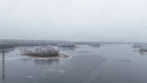 Frozen Rubikiai Lake in Lithuania on a foggy winter day. Aerial view of the frozen Rubikiai Lake in Lithuania, with snow-covered islands and foggy winter skies creating a serene scene. photo