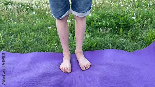 Child slowly transfers body weight from one foot to the other while standing barefoot on a purple yoga mat in the grass, dirty feets