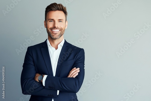 Smiling man in a navy suit with arms crossed against a light grey background, professional studio portrait with soft lighting and sharp focus.