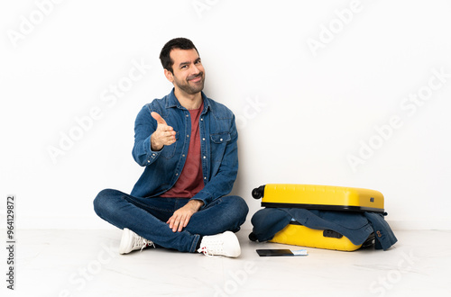 Caucasian handsome man with a suitcase full of clothes sitting on the floor at indoors shaking hands for closing a good deal