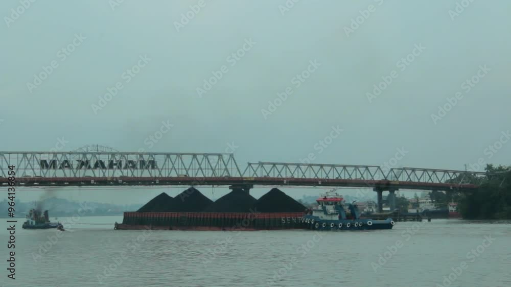 Dramatic view of a coal barge passing under the Mahakam Bridge. Dramatic view of a coal barge passing under the Mahakam Bridge.