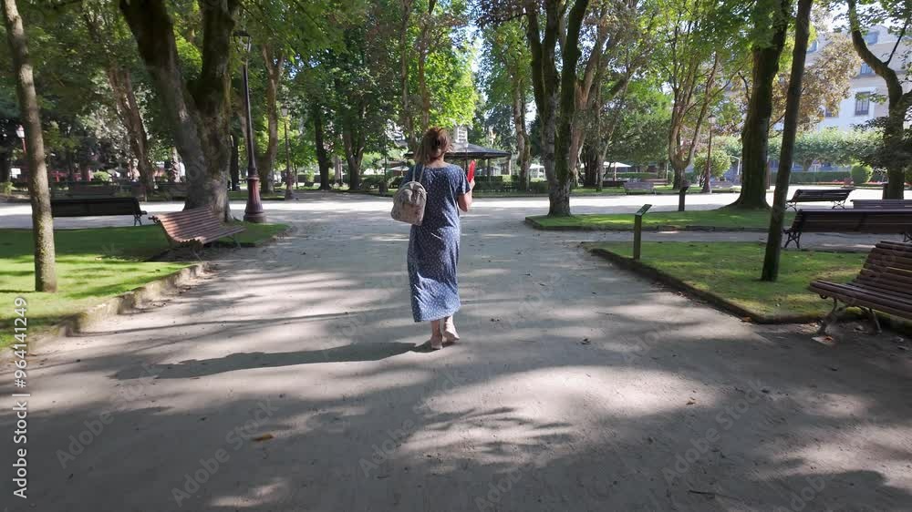 Woman in a dress walking through a public park and fanning herself on a hot day, Lugo, Galicia. Woman in a dress walking through a public park and fanning herself on a hot day, Lugo, Galicia.