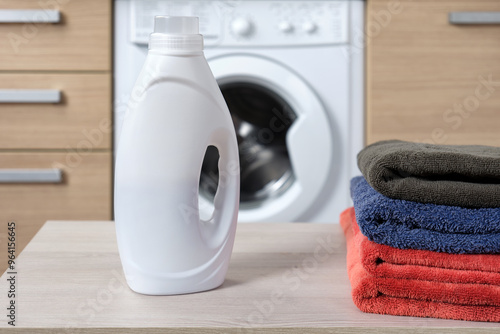 Close-up white plastic bottle with liquid washing gel into the container and many colorful towels. photo