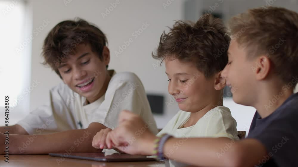 Three boys are gathered around a tablet, sharing laughter as they interact with the screen. Their expressions convey happiness and excitement in a warm, inviting space. Three boys are gathered around a tablet, sharing laughter as they interact with the screen. Their expressions convey happiness and excitement in a warm, inviting space.
