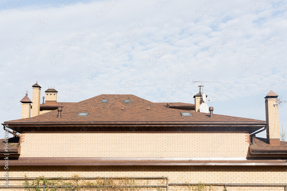 Naklejka premium modern residential brick house with a detailed view of its roof featuring multiple chimneys, skylights, and a clear blue sky in the background