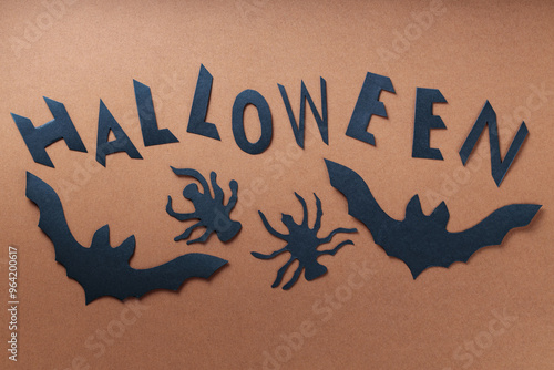 Black Paper Cutouts of Bats, Spiders and Word Halloween on Brown Background, Halloween Concept photo