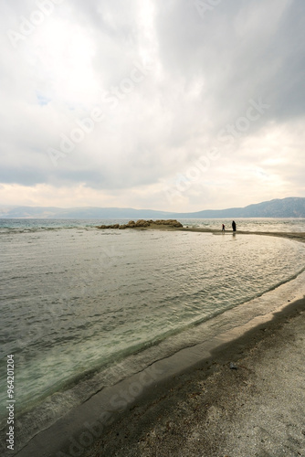 Obraz na płótnie A view of Lake Salda, Turkey, showcases a crescent-shaped bay with pristine white sand and clear turquoise waters. Dark storm clouds loom overhead, adding a dramatic touch to the scene. w salonie