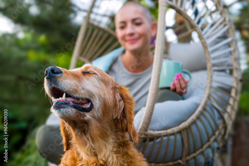 Wallpaper Mural Young female cancer patient relaxing smiling in hanging chair on the patio with her emotional support therapy dog sitting by her side. Mental wellbeing during illness. Torontodigital.ca