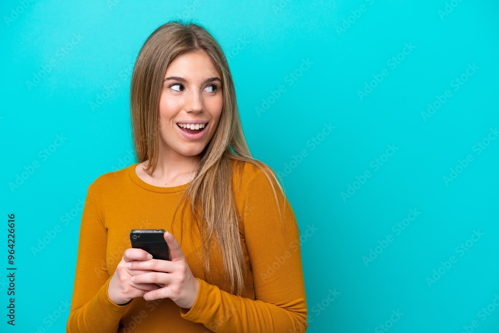 Young caucasian woman isolated on blue background using mobile phone and looking up Young caucasian woman isolated on blue background using mobile phone and looking up