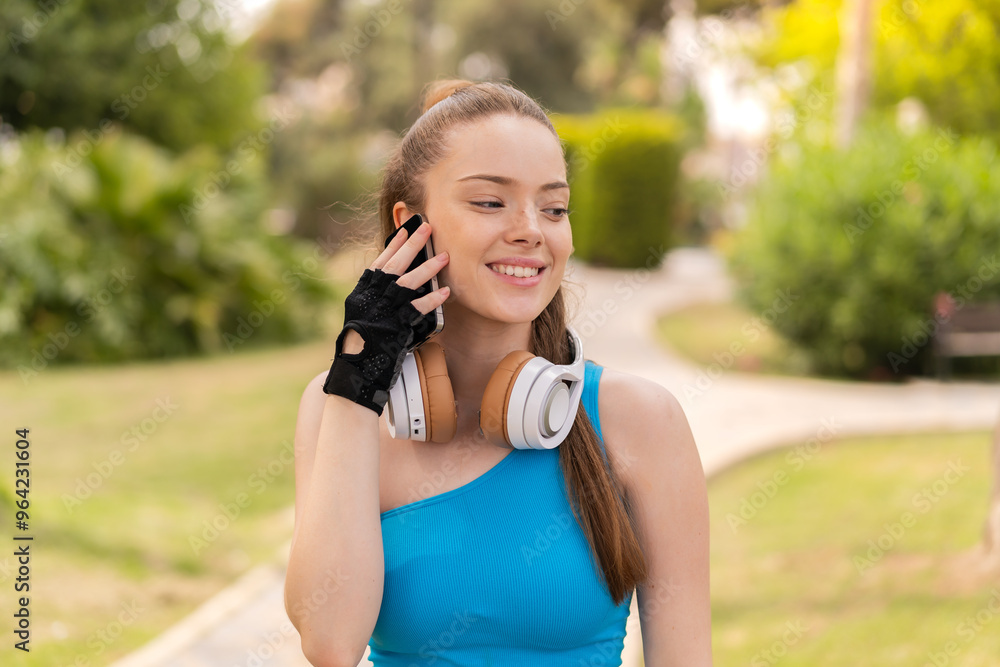 Young pretty girl at outdoors wearing sport wear and keeping a conversation with the mobile phone Young pretty girl at outdoors wearing sport wear and keeping a conversation with the mobile phone