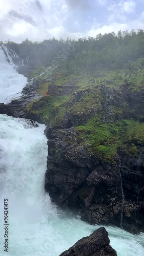 Vertical video, panning shot. Powerfull Kjosfossen waterfall in Western Norway, woman in red dress shows up from behind ruins. photo