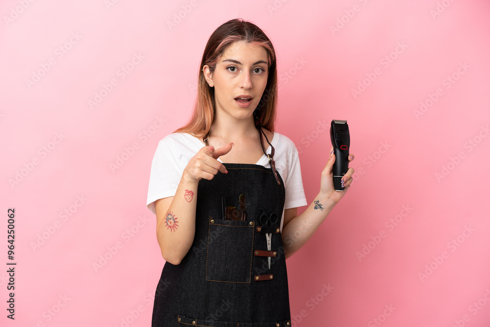 Young hairdresser woman isolated on pink background surprised and pointing front Young hairdresser woman isolated on pink background surprised and pointing front