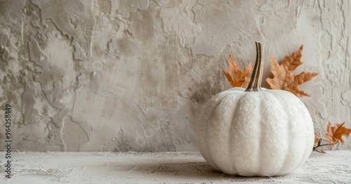 A rustic white pumpkin placed in front of a textured wall with scattered autumn leaves nearby, creating a seasonal and warm decor setting. Halloween and Thanksgiving concept.  photo