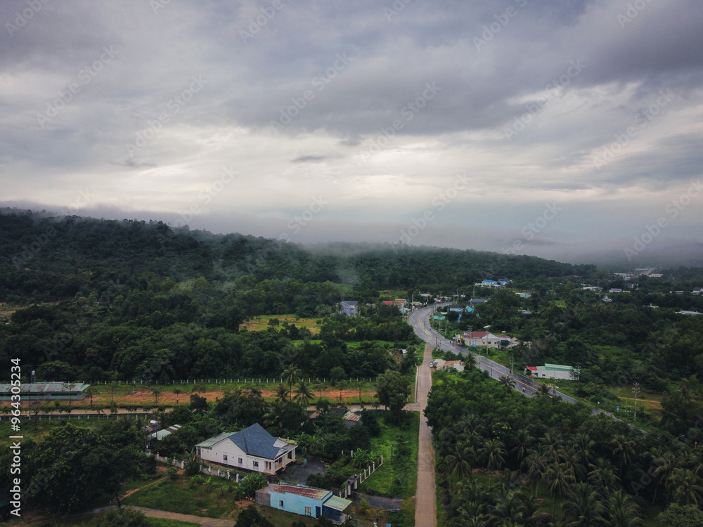 Aerial shot in the outskirts of Le Bat, Phu Quoc, Vietnam. A small town can be seen, surrounded with rainforest with a road cutting through the middle. Traditional wooden houses can be seen Aerial shot in the outskirts of Le Bat, Phu Quoc, Vietnam. A small town can be seen, surrounded with rainforest with a road cutting through the middle. Traditional wooden houses can be seen