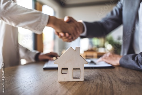 Wooden model house on table, handshake in blurred background, natural light setting