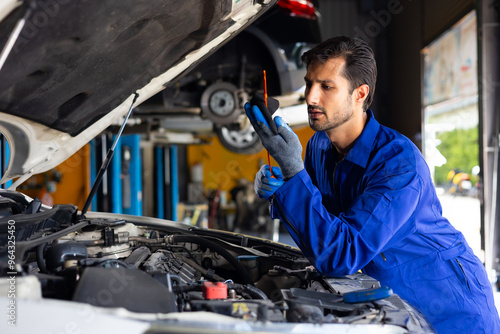 hispanic latin male mechanic repairs car in garage. Closeup hand. Auto car mechanic checking the oil level of the car engine. Car repair and maintenance