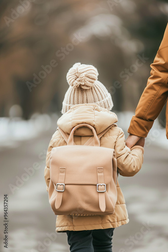 A child wearing a white hat and a brown jacket is walking with a parent