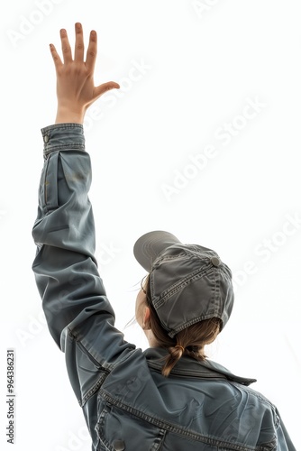 A woman in a denim jacket and cap reaches her hand upwards, looking at something out of frame.