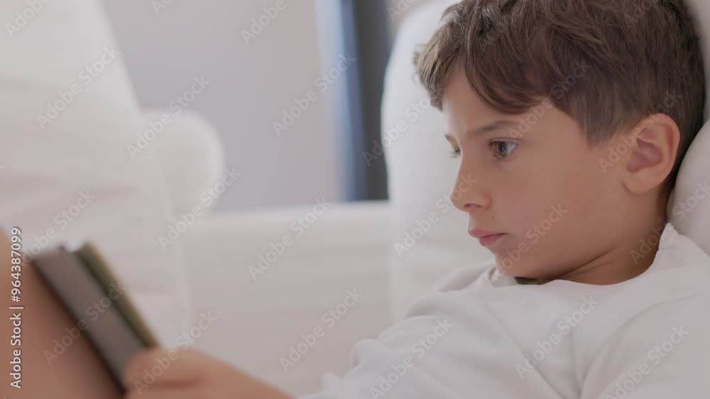 A child comfortably lies on a soft sofa, deeply focused on reading a book in a bright, airy room filled with natural light. A child comfortably lies on a soft sofa, deeply focused on reading a book in a bright, airy room filled with natural light.