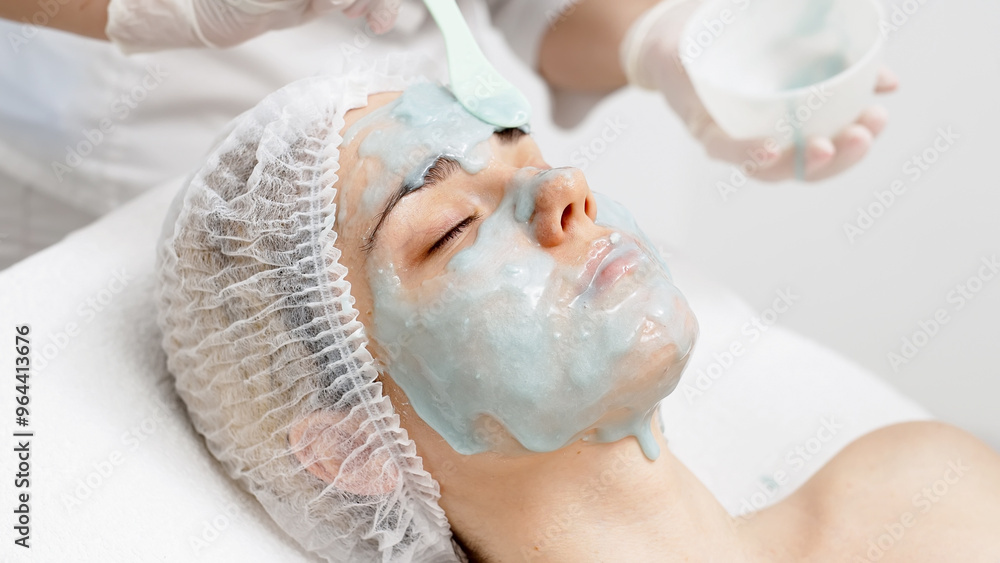 A cosmetologist applies an alginate face mask on a young woman in a modern salon. This treatment boosts skin hydration and rejuvenation, perfect for highlighting premium skincare in your ads. A cosmetologist applies an alginate face mask on a young woman in a modern salon. This treatment boosts skin hydration and rejuvenation, perfect for highlighting premium skincare in your ads.