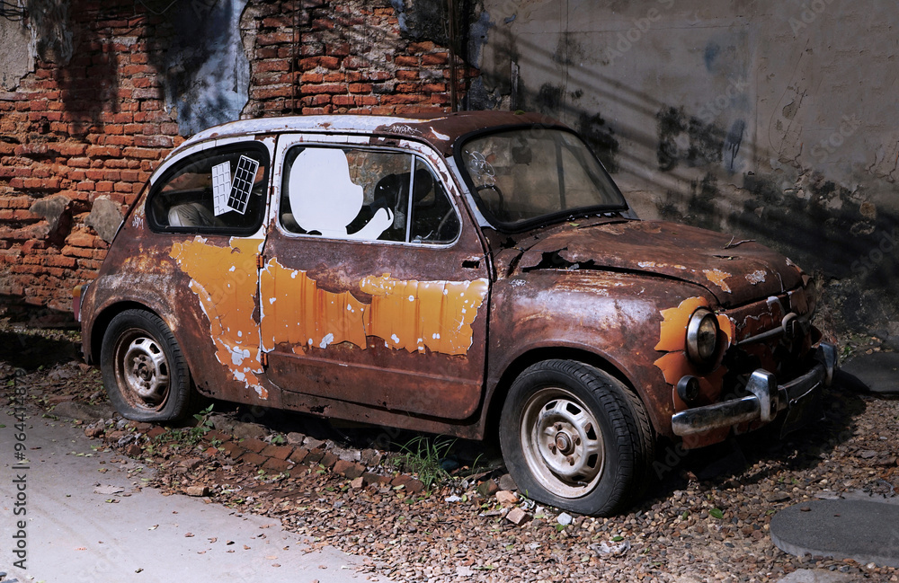 Fototapeta premium Old Orange car wrecks parked against a brick wall on a walkway in a tourist attraction in Bangkok.