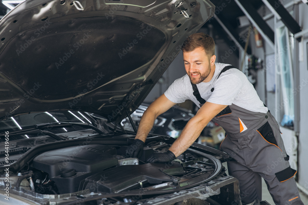 Smiling Auto Mechanic in Overalls Working on Car Engine in Garage Smiling Auto Mechanic in Overalls Working on Car Engine in Garage