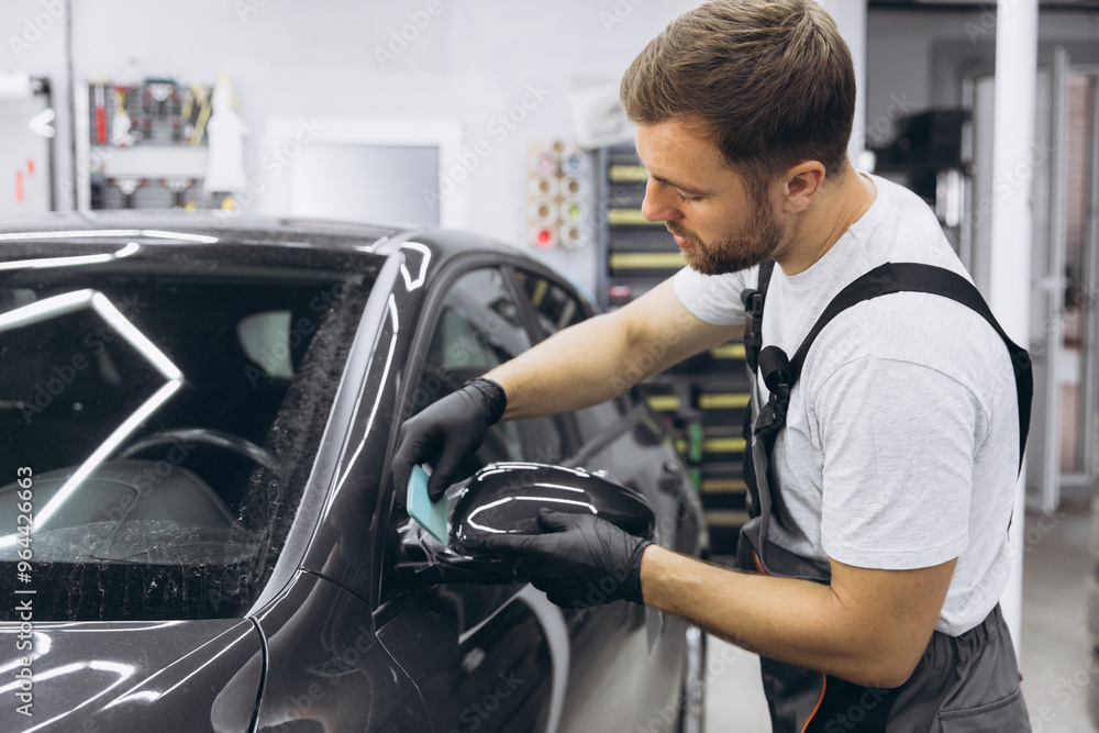 Professional Auto Mechanic Applying Protective Film to Car Mirror in Workshop Professional Auto Mechanic Applying Protective Film to Car Mirror in Workshop