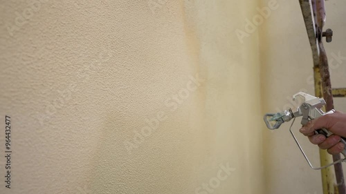 Construction worker painting wall using spray gun.