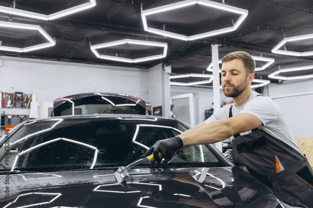 Man washing car hood and preparing the polishing process Car glass coating. Male worker installing protection film to car in garage. Car Detailing. Man washing car hood and preparing the polishing process Car glass coating. Male worker installing protection film to car in garage. Car Detailing.