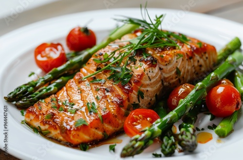 Delicious grilled salmon served with fresh asparagus and cherry tomatoes on a white plate, garnished with herbs.