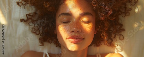 A person with a relaxed smile, lying down with eyes closed and basking in the warm sunlight against a white backdrop.