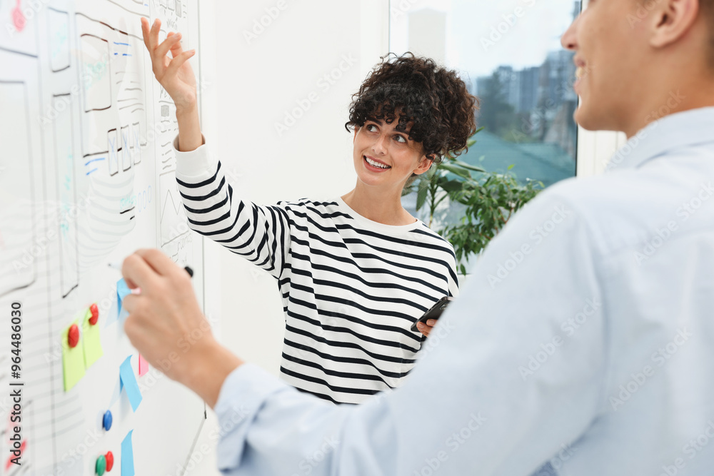 Developing UI design. Man and woman drawing website wireframe on whiteboard indoors Developing UI design. Man and woman drawing website wireframe on whiteboard indoors