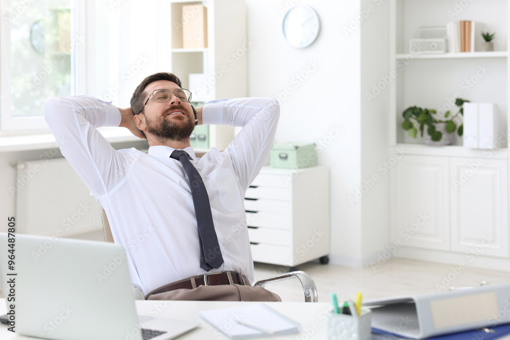 Smiling businessman sitting at table in office with hands behind his head. Break time Smiling businessman sitting at table in office with hands behind his head. Break time