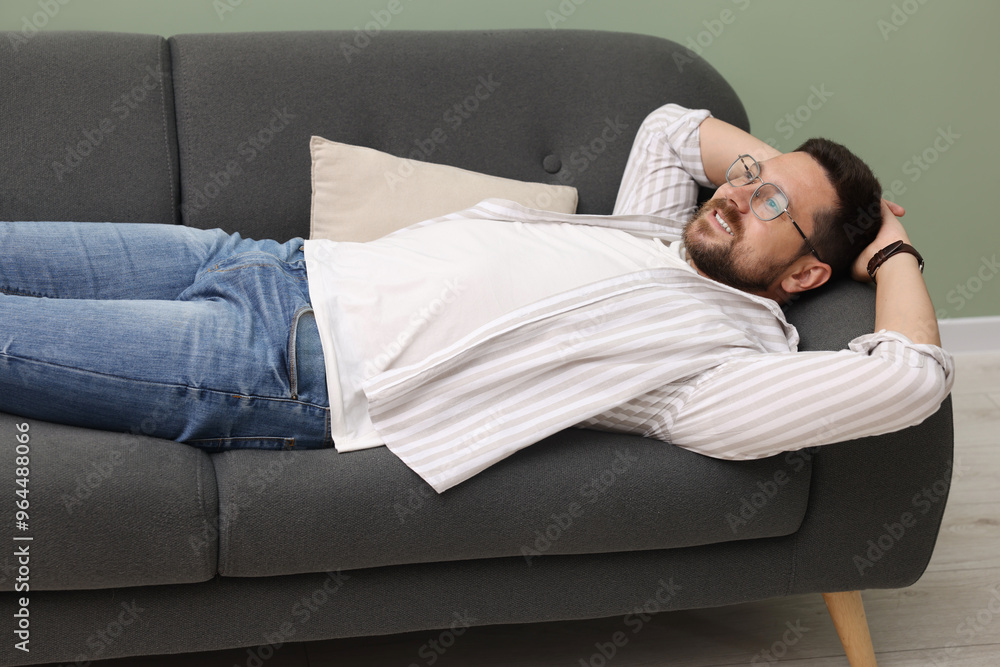 Smiling man with hands behind his head relaxing on sofa at home Smiling man with hands behind his head relaxing on sofa at home